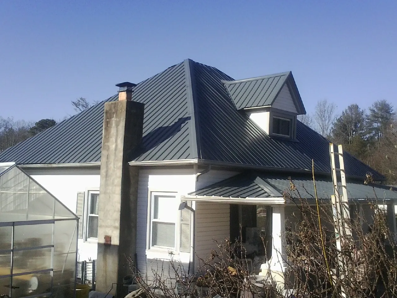 Dark blue standing seam metal roof on a white farmhouse with dormer — Slate & Tile Roof Repair by Roofing Brothers in East Rochester