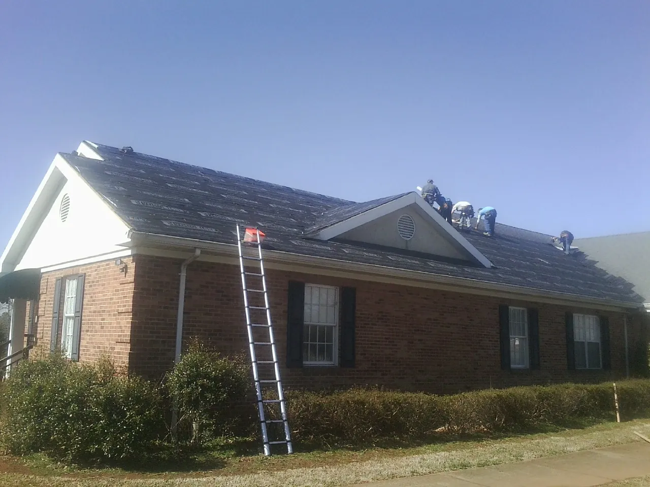 Crew tearing shingles off a brick ranch roof with a ladder set — Metal Roof Repair work by our crew in East Rochester