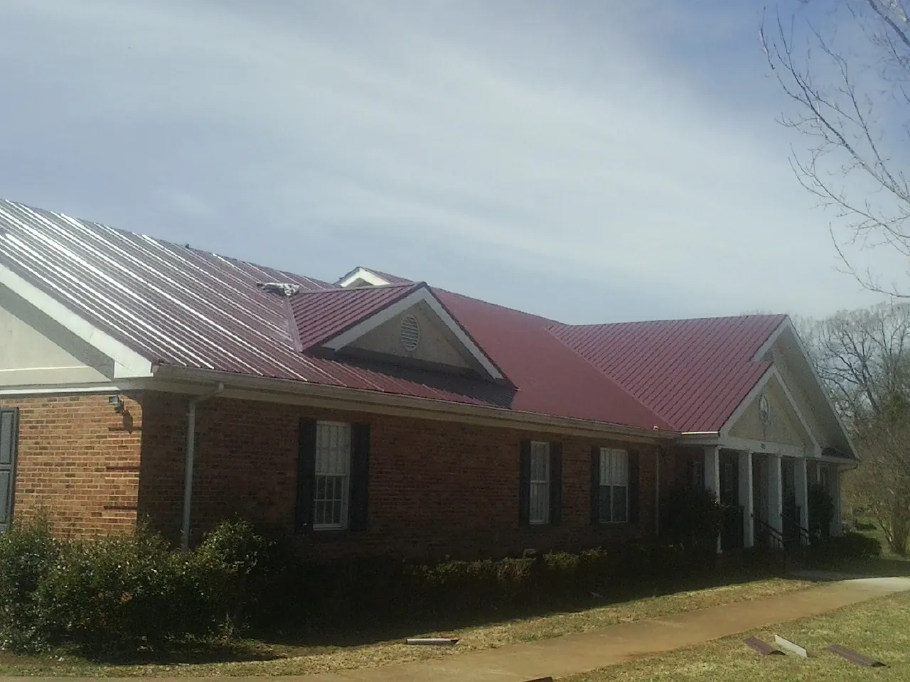 Red metal roof with gabled entries on a long brick building, from a Hail Damage Roof Repair job in East Rochester