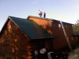 Crew on the ridge of a green metal roof on a two story log home in East Rochester