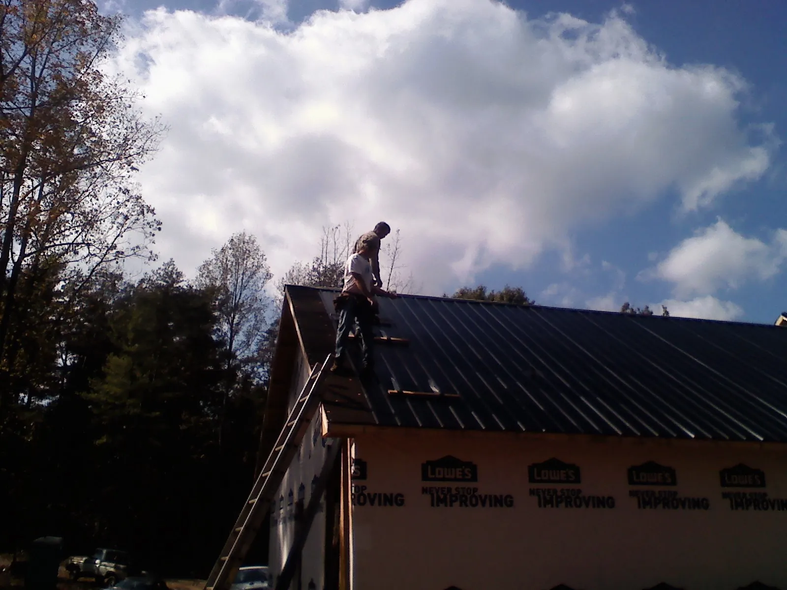 Roofer fastening dark metal panels high against a cloudy sky, from a Roof Inspection job in East Rochester